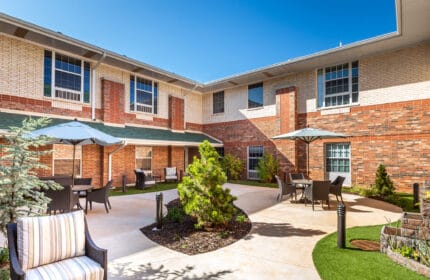 Spanish Cove Retirement Community Exterior of Building with Courtyard Seating, Umbrella-covered Tables