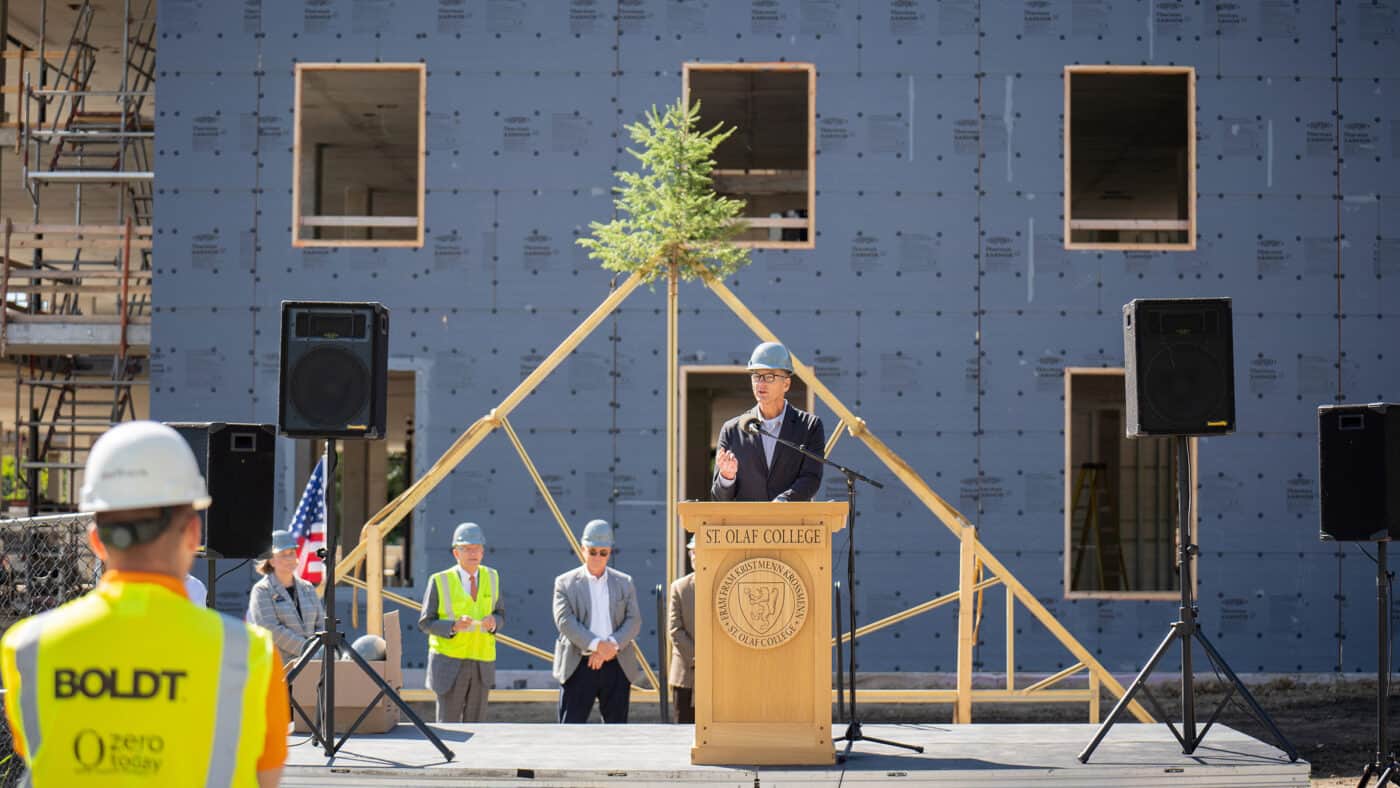 St. Olaf College - Residence Hall Construction Event with Boldt Employee in Foreground Wearing Safety Vest as Tom Boldt Looks at Stage