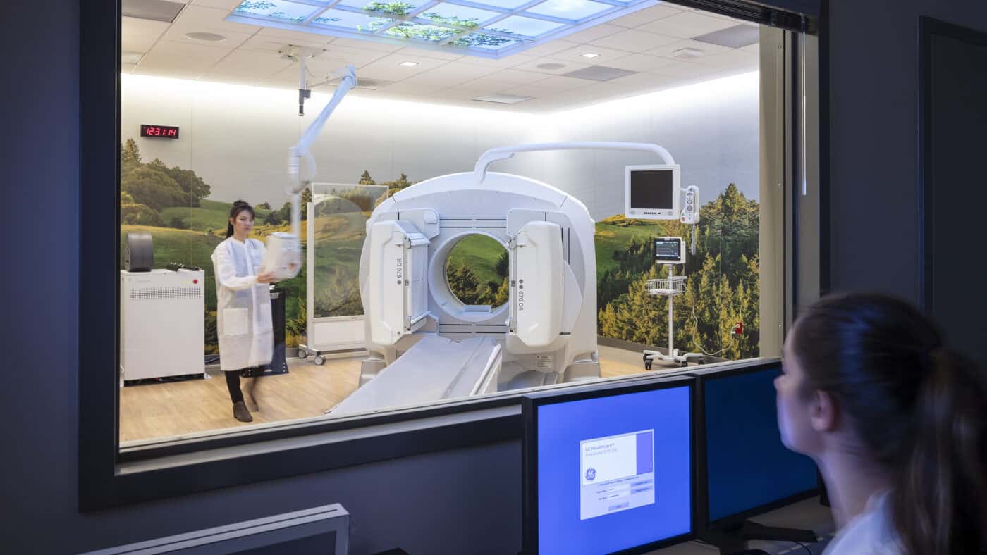 Sutter Health CMPC Van Ness Campus Hospital - Imaging Equipment Shown from Viewing Room with Employee in Imaging Room and Viewing Room