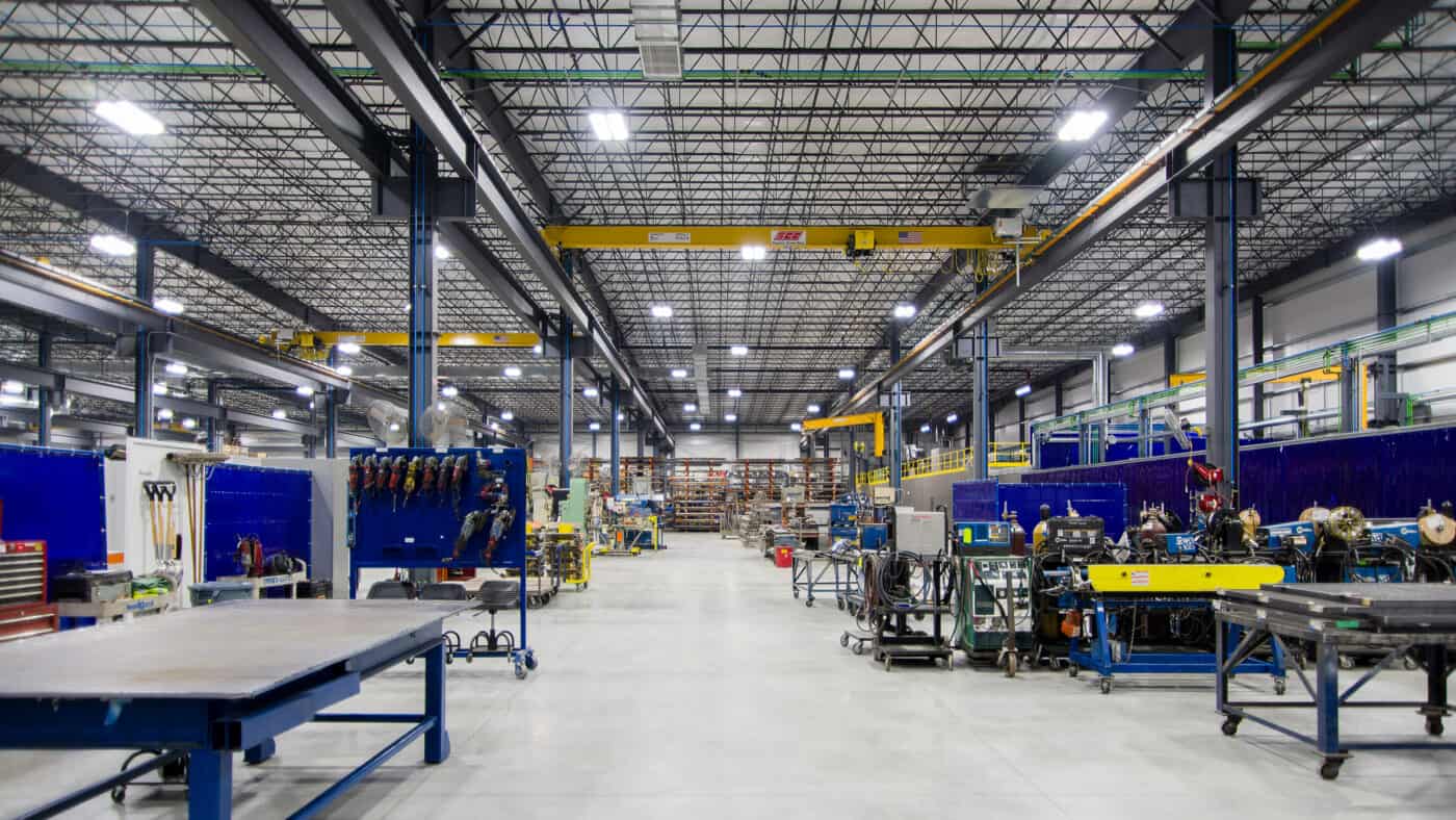 Tweet/Garot Production Facility Interior View of Walkway Between Workstations with Exposed Structural Steel Beams and High Ceilings, Overhead Lifts